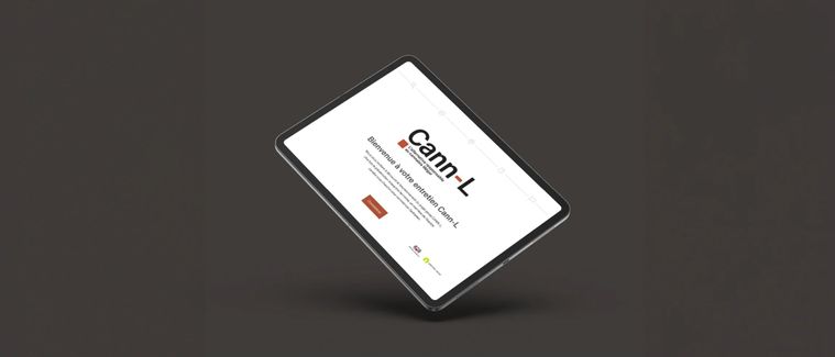Tablette posée en biais sur fond gris anthracite, affichant l'accueil de la plateforme Cann-L avec son titre et un bouton rouge brique.